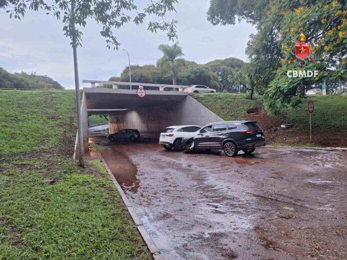 Imagem de operação do Corpo de Bombeiros do DF em alagamento na 210 Sul, com veículos parcialmente submersos.