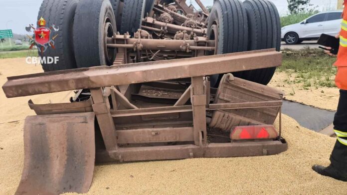 Imagem de carreta tombada na DF-130 em Planaltina com carga de soja espalhada fora da pista
